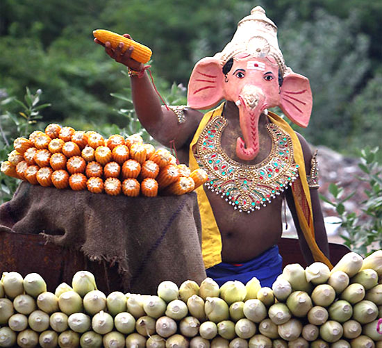 A man, wearing a mask of Hindu god Ganesh, the deity of prosperity, holds up a cob of corn at a roadside stall on the fourth day of the Ganesha Chaturthi festival in Chennai.