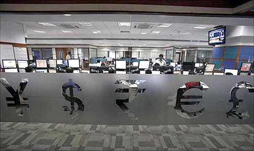 Foreign currency traders work inside a trading firm behind the signs of various world currencies in Mumbai.