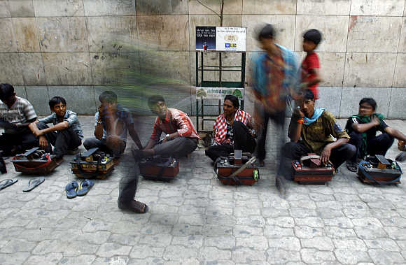 A commuter walks past cobblers sitting in a line waiting for customers outside a metro station in New Delhi.