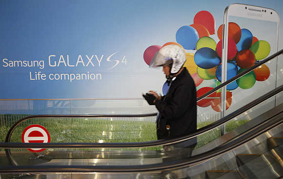 A motorcycle dispatch rider uses his smartphone next to an advertisement promoting Samsung Galaxy S4 smartphone at the company's headquarters in Seoul, South Korea.