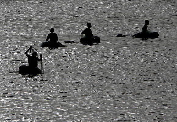 Fishermen floating on rubber air tubes are silhouetted as they catch fish in the waters of the Sabarmati river in Ahmedabad.