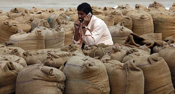 A man speaks on a mobile phone amid sacks filled with wheat and rice in Ahmedabad.