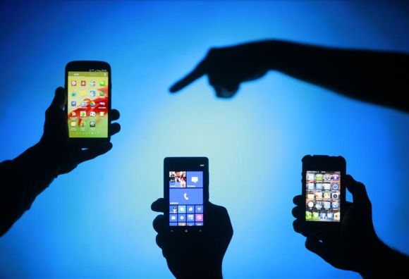 Men are silhouetted against a video screen as they pose different smartphones.
