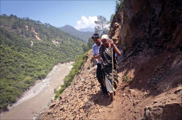 A pilgrim is helped by a villager as she tries to cross on a pathway damaged by landslide in Rudraprayag in Uttarakhand.