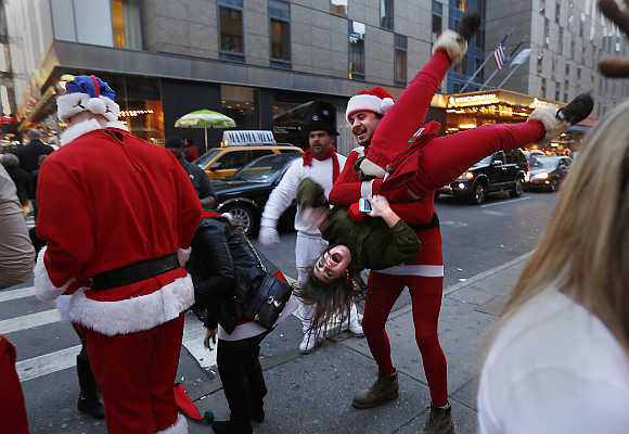 A man carries a woman upside down as other revelers walk down 8th Avenue during SantaCon in New York City.