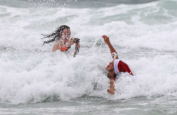 A woman enjoys the waves as her friend takes pictures on a cold and rainy Christmas day on Bondi Beach in Sydney, Australia.