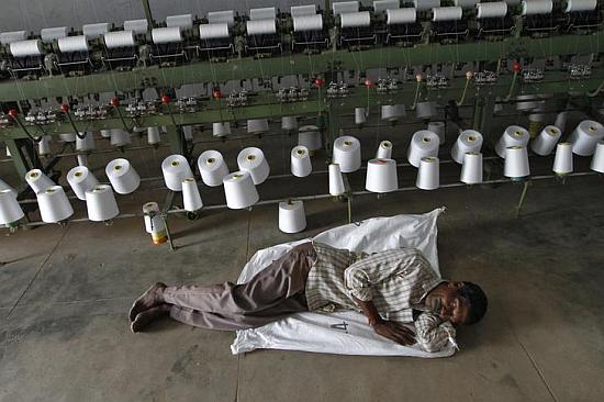 A worker takes a nap during a power cut in front of yarn-spinning equipment inside a factory in Coimbatore.