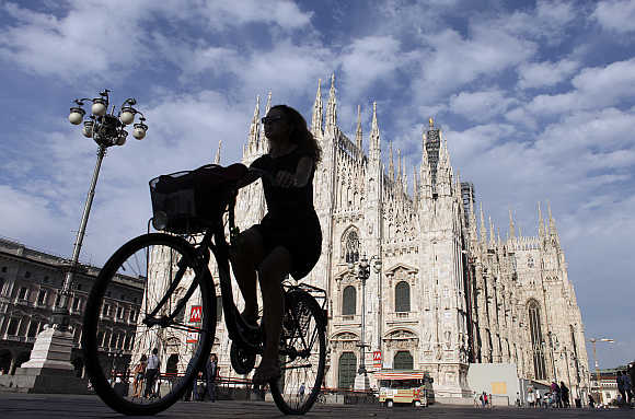 A woman rides a bicycle in front of the Duomo cathedral in downtown Milan, Italy.
