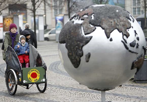 A woman rides a bicycle past a globe in downtown Copenhagen, Denmark.
