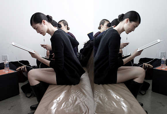 A model is reflected in a mirror while she reads her iPad backstage before a fashion show in New York City.