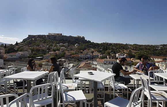 People sit in a cafe with the Acropolis hill in the background in central Athens, Greece.