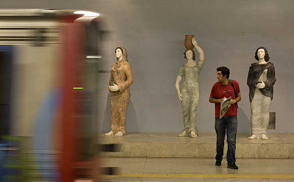 A subway passenger watches the arrival of a train in front of marble statues of traditional figures in Lisbon, Portugal.