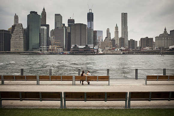 A couple sits on a bench in Brooklyn Bridge Park, along the East River in New York.