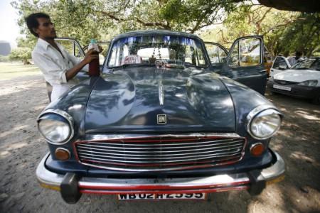 A driver stands next to his parked Ambassador car, manufactured by Hindustan Motors, in Kolkata.