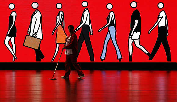 A cleaner sweeps the floor as she walks past an illuminated sign depicting people walking, at Spain's Santander headquarters in Boadilla del Monte outside Madrid.