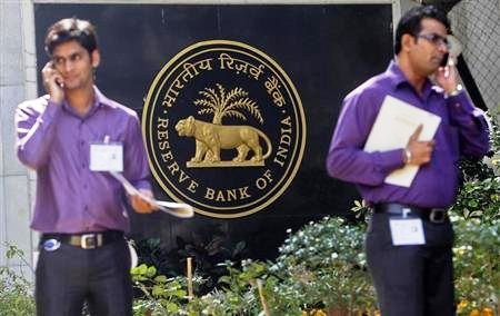 Two men make phone calls while standing near a Reserve Bank of India crest at the RBI headquarters in Mumbai.