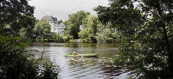 A man in a canoe paddles on a stretch of water leading to inner city lake Alster on a sunny day in Hamburg, Germany.