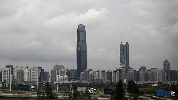 Container trucks cross a bridge in front of the 100-floor Kingkey 100, the tallest building in downtown Shenzhen, China.