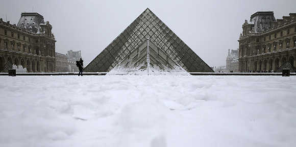 People enjoy the snow in front of Paris landmark, the Pyramid of the Louvre Museum, in France.