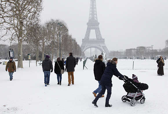 People walk in groups on a snow-covered path near the Eiffel Tower in Paris, France.
