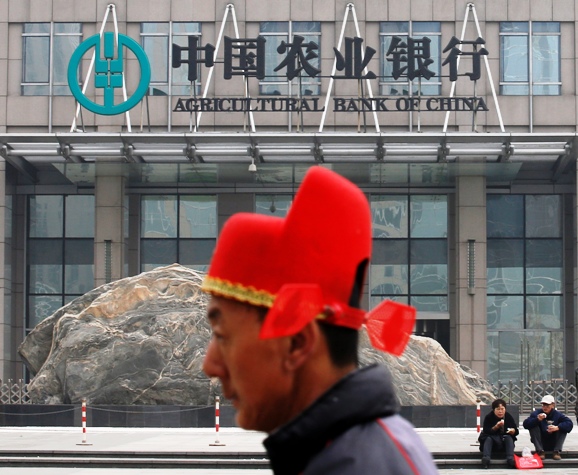 A man wearing a traditional Chinese hat walks past the headquarters of the Agricultural Bank of China in Beijing.