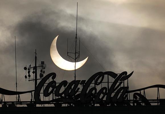 A partial solar eclipse is visible behind a Coca-Cola signage.
