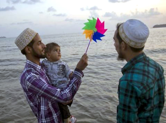 Mohammed (L), 25, holds a paper windmill aloft as he wades in the waters of the Arabian Sea with his son Mortaza and brother Taher in Mumbai.