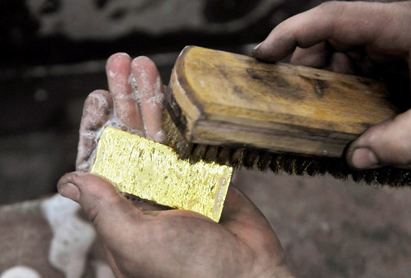 A worker brushes a gold bar.