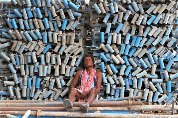 A worker takes a nap beside a stack of iron pipes at the construction site of a commercial complex in Chennai.