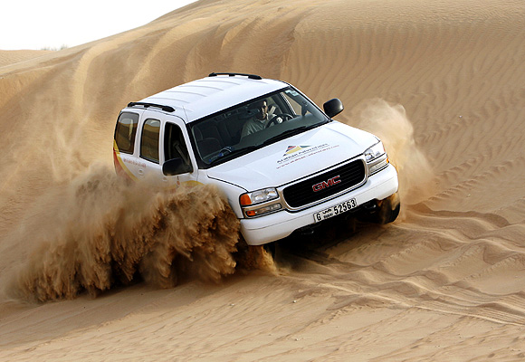 A four-wheel vehicle carrying tourists drives down a dune in the Dubai desert.