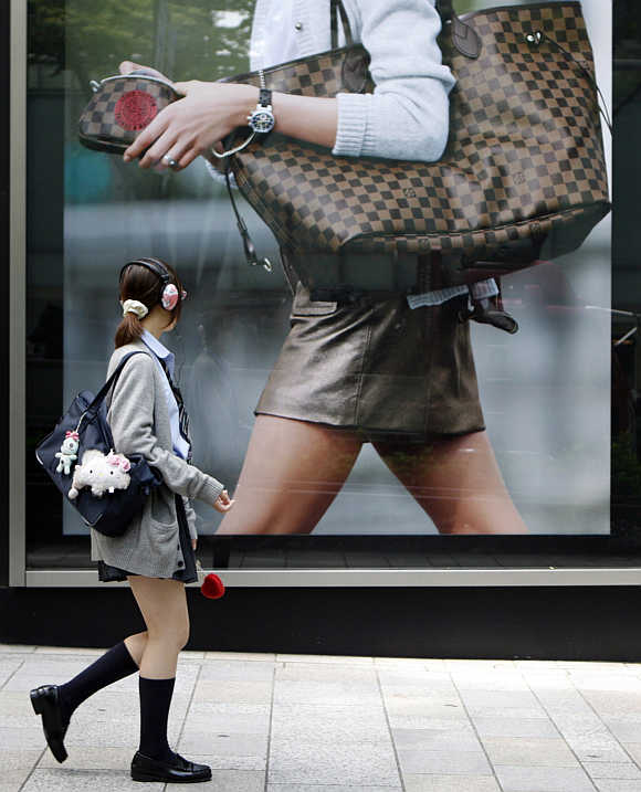 A student in a school uniform walks past a luxury brand store in a Tokyo shopping district, Japan.