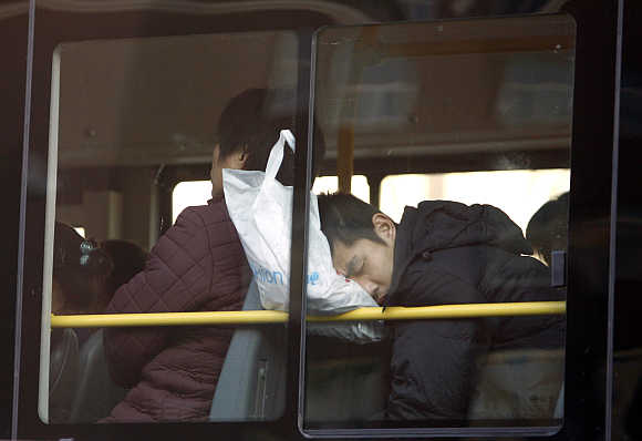A commuter on a public bus sleeps while resting his head on a shopping bag in central Beijing, China.