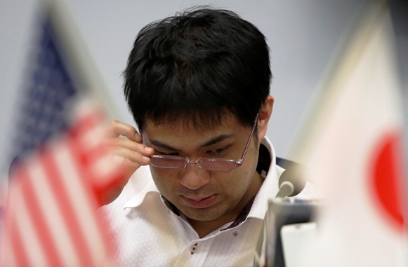 An employee of a foreign exchange trading company adjusts his glasses between the U.S. and Japanese national flags in Tokyo.