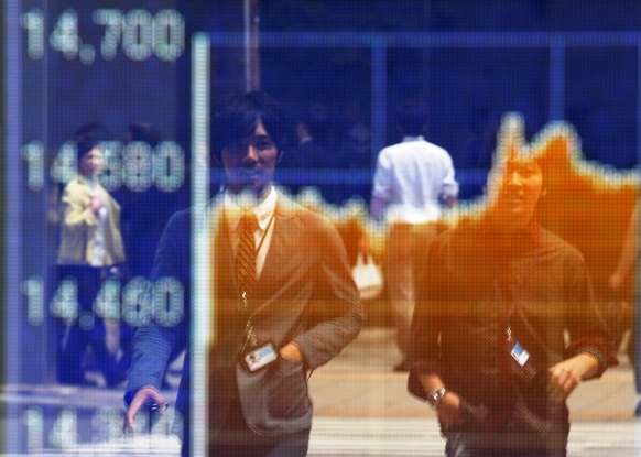 Passersby are reflected on an electronic board displaying a graph showing recent movements of Japanese market indices outside a brokerage in Tokyo.