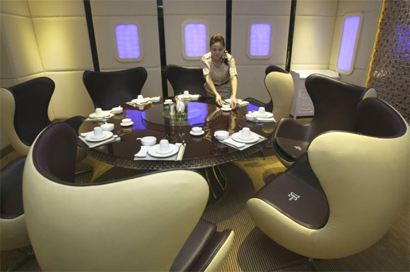 A waitress poses as she arranges a dining table inside a private room of an A380 theme restaurant.