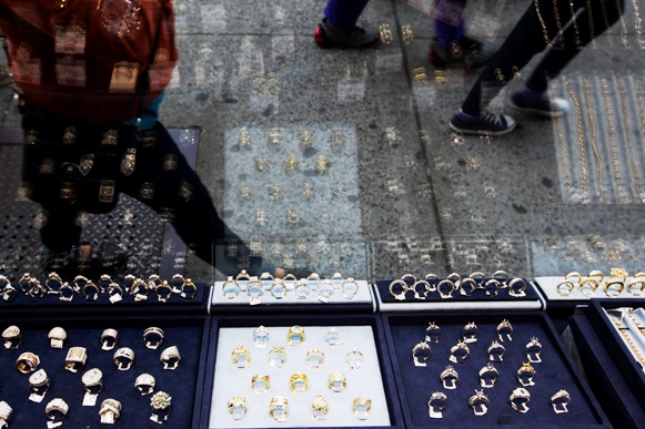 Pedestrians walk past gold and silver jewellery displayed in the window of the Gold Standard jewellery store specializing in purchasing raw gold and silver in New York.