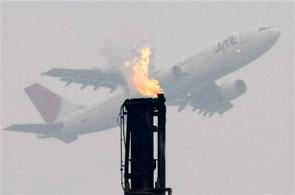 An airplane flies near a gas flare from a factory.