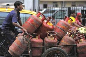 An employee of a cooking gas agency transports gas cylinders on a cart.