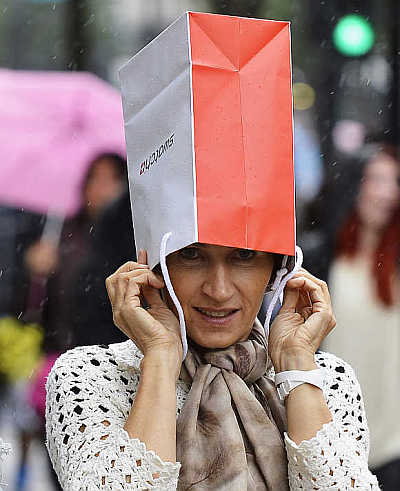 A woman covers her head with a shopping bag to protect herself from rain on Oxford Street in central London, United Kingdom.