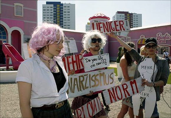 Demonstrators protest with a performance against a Barbie Dreamhouse.
