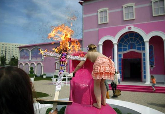 Activists from women's rights group Femen burn a barbie doll on a cross as they protest outside the Barbie Dreamhouse.