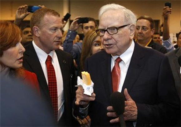 Berkshire Hathaway Chairman Warren Buffett holds a Dairy Queen ice cream bar and answers reporters' questions as his wanders the company trade show before the Berkshire Hathaway annual meeting in Omaha.