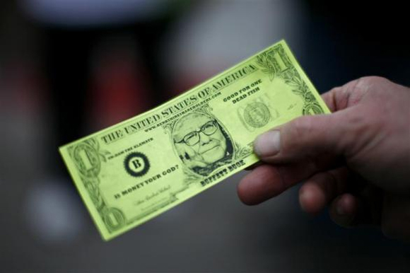 A Berkshire Hathaway shareholder hold a fake dollar bill with the face of billionaire financier and Berkshire Hathaway CEO Warren Buffett during the kick-off celebration at the annual Berkshire Hathaway shareholders meeting in Omaha.
