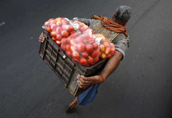 A labourer carrying tomatoes walks along a roadside near a wholesale vegetable market in the old quarters of Delhi.