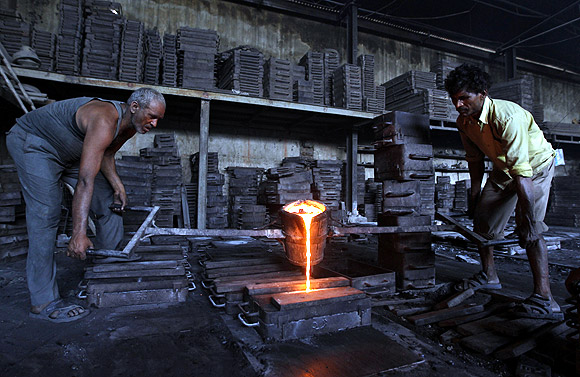 Workers lift a container filled with molten iron inside an iron casting unit at an industrial estate in Ahmedabad.