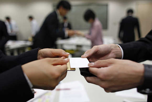 Job-hunting students dressed in suits practice swapping business cards during a business manners seminar at a placement centre in Tokyo, Japan.