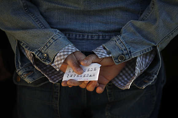 A man holds a paper with a job offer which reads, 'You might want to', as he waits in line to enter a government job centre in Malaga, southern Spain.