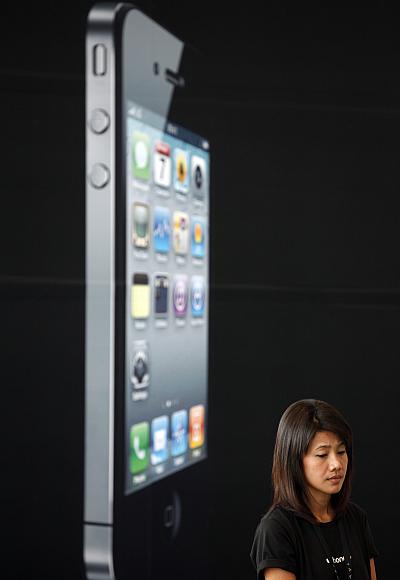 A woman stands next to a giant advertisement for an iPhone in Bangkok.