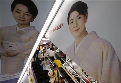 People ride an escalator past Japanese display maker Sharp Corp