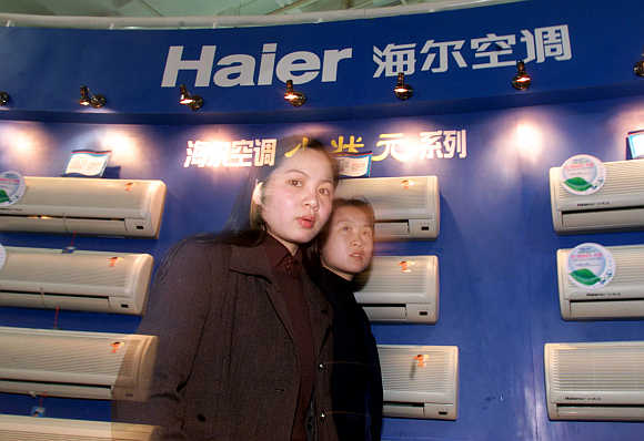 Women pass air conditioners made by China's Qingdao Haier Group in Beijing.